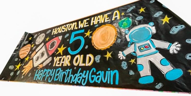 May include: A black banner with a space theme. It says "Houston, we have a 5 year old. Happy Birthday Gavin." There is a rocket, planets, stars, and an astronaut.
