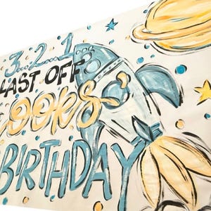 May include: A white banner with a blue and yellow space-themed design. It says "Blast Off Brookes 3rd Birthday" with a rocket ship and planets.