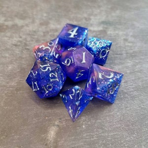 May include: A set of six iridescent dice with silver glitter and white numbers. The dice are in shades of blue and purple.