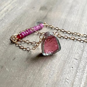 May include: A delicate gold chain necklace with a pink tourmaline pendant and a row of pink sapphires.