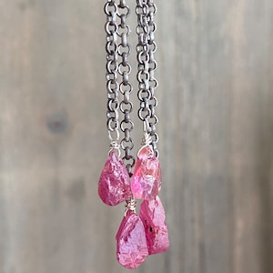 May include: A silver chain necklace with three pink gemstone pendants. The gemstones are rough and have a natural, raw look.
