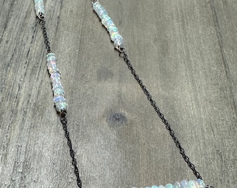 May include: A long silver chain necklace with multiple strands of iridescent white opal beads. The necklace is on a wooden surface.