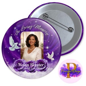 May include: A purple button with a photo of a woman, doves, and roses. Text reads "In Loving Memory" and "Helen Skeeter 12/24/83-1/31/2026". A smaller logo with the text "Proverbs 31 Design" is also visible.