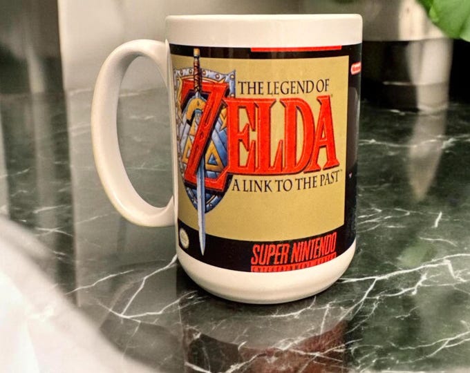Featured listing image: The Legend of Zelda: A Link to the Past Box Art Mug – ALTTP – 15 oz Ceramic – Super Nintendo SNES Cover Design – Video Game Coffee Cup
