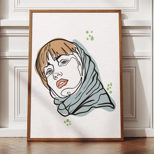 Puede incluir: Una impresión artística enmarcada con un dibujo lineal minimalista del rostro de una mujer. La obra de arte utiliza una línea continua para representar el rostro, con cabello castaño, una bufanda azul claro y labios anaranjados. Puntos verdes dispersos.