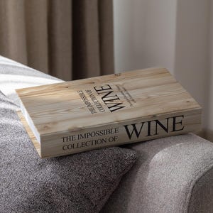 Puede incluir: Una caja de madera con las palabras "WINE" y "THE IMPOSSIBLE COLLECTION OF" impresas en negro. La caja está sobre un sofá gris. La caja tiene un acabado de veta de madera clara.
