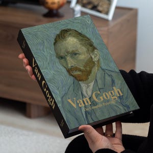 Könnte beinhalten: Ein Hardcover-Buch mit dem Titel "Van Gogh The Complete Paintings" mit einem Porträt von Vincent van Gogh auf dem Cover. Das Buch hat einen schwarzen Buchrücken mit dem Namen des Künstlers in goldener Schrift. Das Cover ist überwiegend blau und grün.