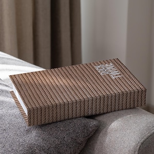 May include: A rectangular box with a rope-like pattern in shades of brown and tan. The box is resting on a gray sofa and has the word "TIME" in white on the top. The box is open, revealing a white interior.
