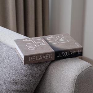 May include: Two hardcover books stacked on top of each other. The top book is brown with white text that reads "RELAXED LUXURY". The bottom book is black with white text that reads "RELAXED LUXURY".