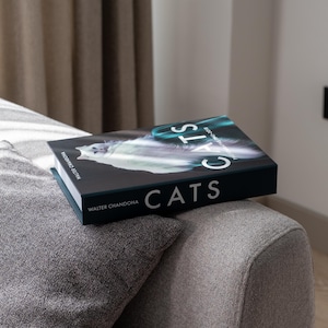 Puede incluir: Un libro de tapa dura titulado "CATS" de Walter Chandoha. La portada del libro presenta un gato blanco con un fondo negro y la palabra "CATS" en letras blancas.