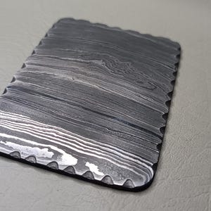 Puede incluir: Un tarjetero rectangular y texturizado con un patrón único de líneas grises y blancas arremolinadas. Los bordes están festoneados y delineados en negro. El tarjetero está hecho de un material duradero.