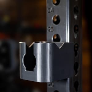 May include: A black metal weight plate holder attached to a weight rack. The holder has a rectangular shape with a round opening in the center.