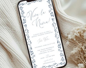 Puede incluir: Un teléfono inteligente muestra una invitación a una despedida de soltera. La invitación presenta el texto "Viva la Novia!" en cursiva, rodeado por un borde floral. También incluye el nombre de la homenajeada, la fecha, la hora y el lugar.