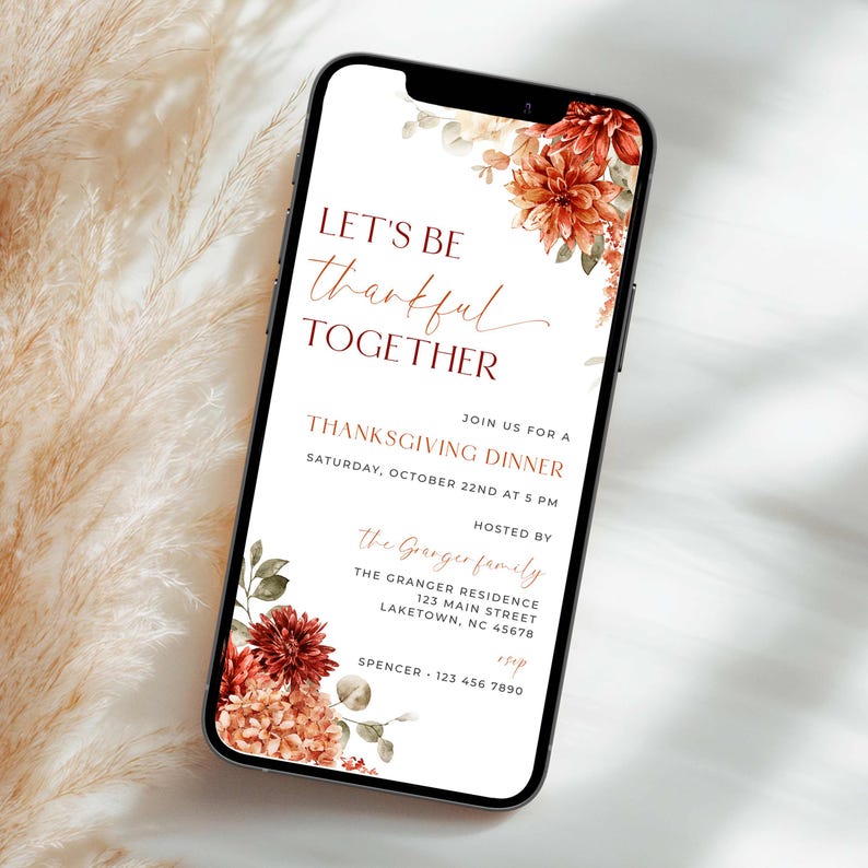 K&ouml;nnte beinhalten: Ein Smartphone zeigt eine Einladung zum Thanksgiving-Dinner. Die Einladung hat florale Akzente in Rot- und Oranget&ouml;nen mit dem Text "LET'S BE thankful TOGETHER". Details wie Datum, Uhrzeit und Gastgeberinformationen sind enthalten.