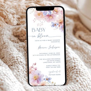 Puede incluir: Un teléfono inteligente muestra una invitación a un baby shower. El diseño presenta arte floral en acuarela en tonos pastel rosas, morados y azules. El texto incluye "BABY in bloom" y detalles del evento.