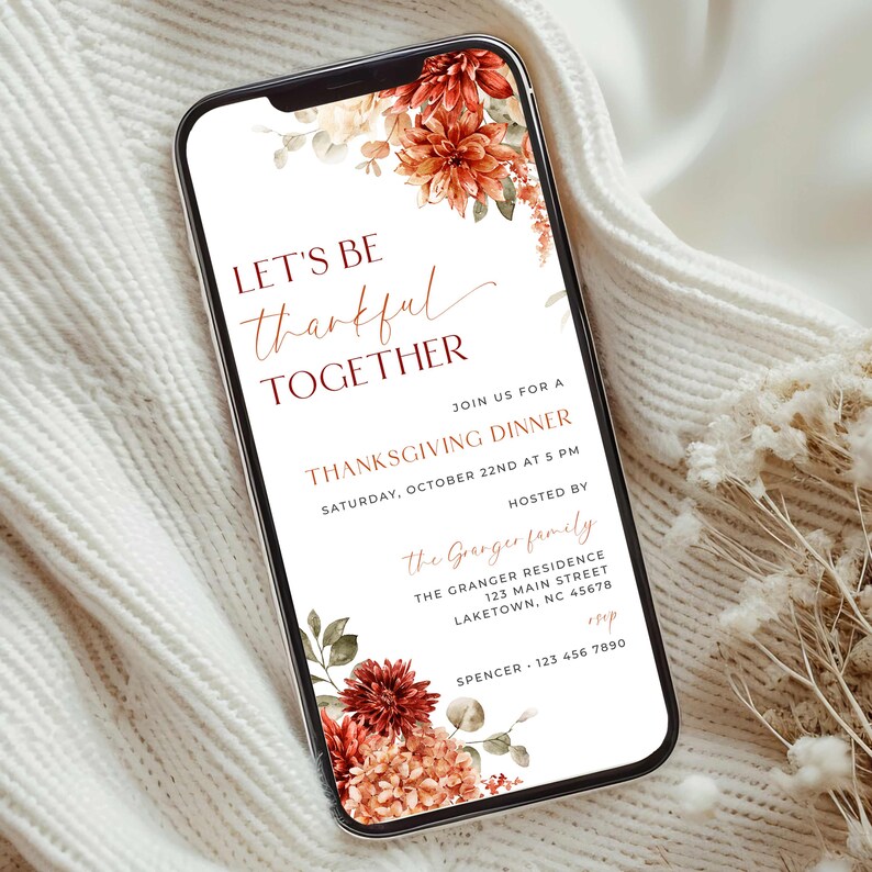 K&ouml;nnte beinhalten: Ein Smartphone zeigt eine Einladung zum Thanksgiving-Dinner. Die Einladung enth&auml;lt den Text "LET'S BE thankful TOGETHER" mit floralen Elementen in Rot-, Orange- und Cremet&ouml;nen. Die Einladung enth&auml;lt Datum, Uhrzeit und Gastgeberdetails.