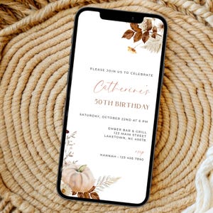 Puede incluir: Un teléfono inteligente muestra una invitación de cumpleaños digital con fondo blanco, detalles florales marrones y una ilustración de calabaza pálida. El texto dice: Please join us to celebrate Catherine's 50th birthday, Saturday, October 22nd at 6 PM, Ember Bar & Grill, 123 Main Street, Laketown, NC 45678, RSVP Hannah 123 456 7890.