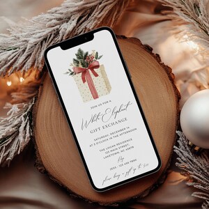 Peut inclure: Un smartphone affichant une invitation num&eacute;rique pour un &eacute;change de cadeaux White Elephant. Le design pr&eacute;sente un coffret cadeau cr&egrave;me &agrave; pois dor&eacute;s, un ruban rouge et des branches de pin. Le texte indique les d&eacute;tails, la date et l'heure.