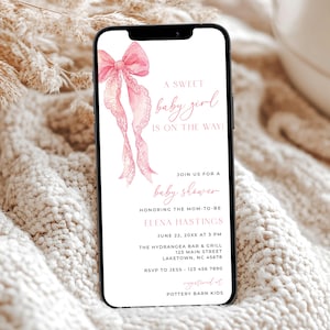 Peut inclure: Un smartphone affiche une invitation à une baby shower. L'invitation présente un nœud rose à l'aquarelle et le texte "A sweet baby girl is on the way !" Les détails incluent le nom de l'invitée d'honneur, la date, l'heure et le lieu.