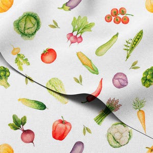 Könnte beinhalten: Weißer Stoff mit einem Aquarellmuster verschiedener Gemüsesorten. Das Design umfasst Tomaten, Radieschen, Mais, Zucchini und Paprika. Weitere Gemüsesorten sind Kohl, Aubergine und Karotten. Der Stoff hat eine leichte, luftige Anmutung.