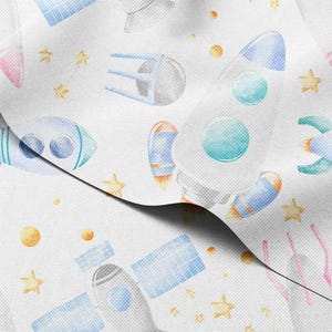 以下が含まれることがあります： 白地の生地に、青、オレンジ、黄色、ピンクの色合いで描かれた水彩画のロケット、衛星、星、惑星の繰り返し模様。 デザインは、気まぐれな宇宙をテーマにした美学を持っています。