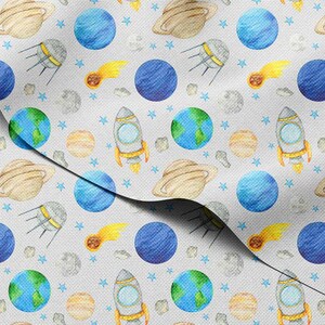 Puede incluir: Una tela gris claro con un patrón repetido de planetas, cohetes, satélites, estrellas y cometas en acuarela. Los planetas son azules, beige y verdes. Los cohetes tienen llamas naranjas.