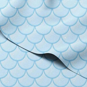May include: Light blue fabric with a repeating pattern of overlapping, rounded shapes resembling mermaid scales. The fabric has a subtle texture and a slight sheen, with a darker blue outline on each scale. The fabric is folded over, revealing the pattern.