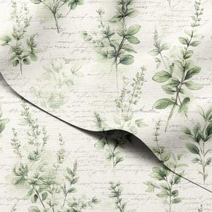 Puede incluir: Tela con motivos botánicos con fondo crema y un patrón de hojas y tallos verdes. El diseño incluye escritura manuscrita en gris descolorido, creando una estética vintage. La tela está doblada, revelando el patrón.