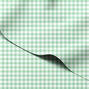May include: A close-up of a green and white gingham pattern fabric. The fabric is folded over, revealing a shadow underneath. The pattern is a classic checkered design, with evenly spaced squares.