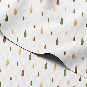 May include: White fabric featuring a repeating pattern of teardrop shapes in brown, green, and yellow. The fabric is folded, showing the texture and pattern. The design is simple and nature-inspired.
