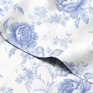 Può includere: Primo piano di un tessuto bianco con un motivo floreale blu. Il design presenta grandi fiori di peonia e rametti floreali più piccoli, creando un'estetica classica ed elegante. Il tessuto è piegato, mostrando la continuità del motivo.