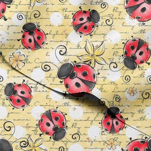May include: A fabric with a repeating pattern of red ladybugs with black spots and black heads on a yellow background. The background has white polka dots, floral accents, and handwritten script.