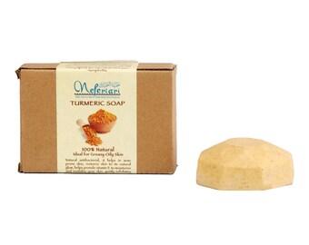 May include: A brown cardboard box with a white label that reads "Mefertari" and "Turmeric Soap". The label also includes a small image of turmeric powder in a bowl. The box is next to a yellow bar of soap.