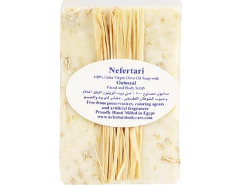May include: A white bar of soap with a label that reads "Nefertari 100% Extra Virgin Olive Oil Soap with Oatmeal Facial and Body Scrub". The soap is wrapped in a natural fiber material.