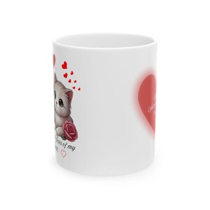 Puede incluir: Taza de cerámica blanca con un gato de dibujos animados, una rosa roja y corazones. La taza tiene el texto "Purr of my heart" y un gran corazón rojo con texto en cursiva. Un regalo temático de San Valentín.