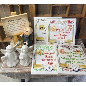 Könnte beinhalten: Satz von fünf weißen Keramikfliesen mit bunten Buchdesigns und religiösem Text. Die Fliesen zeigen verschiedene christliche Gebete, darunter "Gib uns heute unser tägliches Brot" und "Gott segne unser Zuhause heute, morgen und für immer".