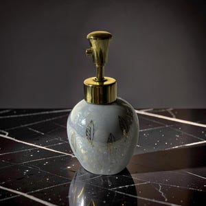 May include: A decorative perfume bottle with a light blue, speckled body and gold accents. The bottle features a gold-colored pump and is adorned with gold leaf designs. The bottle is a unique piece for display.