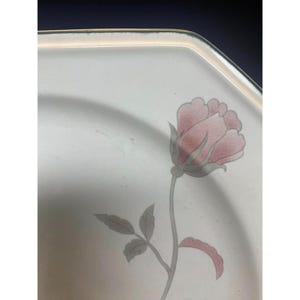 May include: A white octagonal ceramic plate with a green rim features a single pink rose with green leaves and stem.