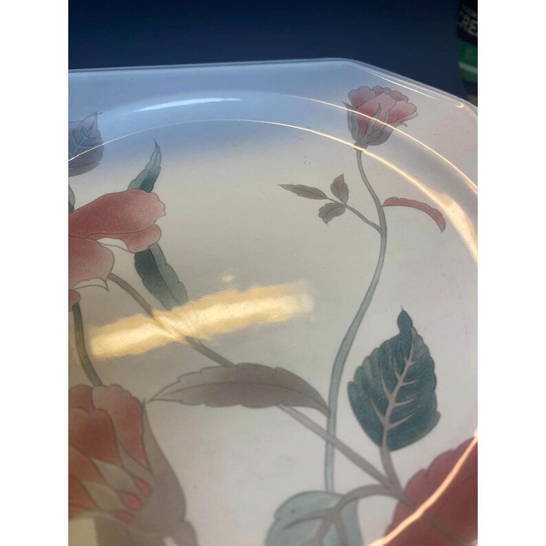 May include: A white ceramic dinner plate with a floral design. The plate features pink and red flowers with green leaves on a white background.