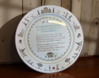 May include: A decorative white plate with a poem and alphabet design. The plate features a border with floral and figure illustrations. The poem includes the text: "It was in this cheery kitchen..." and "When grandma was a little girl..."