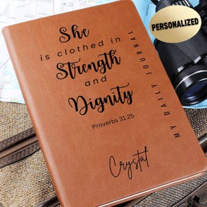 May include: Brown leather journal with the text "She is clothed in Strength and Dignity Proverbs 31:25" and the name "Crystal" written in cursive. The journal has the words "My Daily Journal" written vertically on the spine.