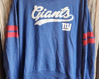 May include: Blue hooded sweatshirt with red and white stripes on the sleeves. The sweatshirt has the word "Giants" in white with a white "NY" logo below it.