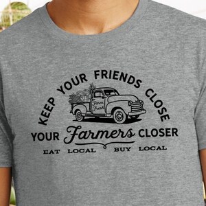 May include: Gray t-shirt with a black graphic of a pickup truck with a sign that says "Farm Fresh" and the text "Keep your friends close, your farmers closer. Eat local, buy local."