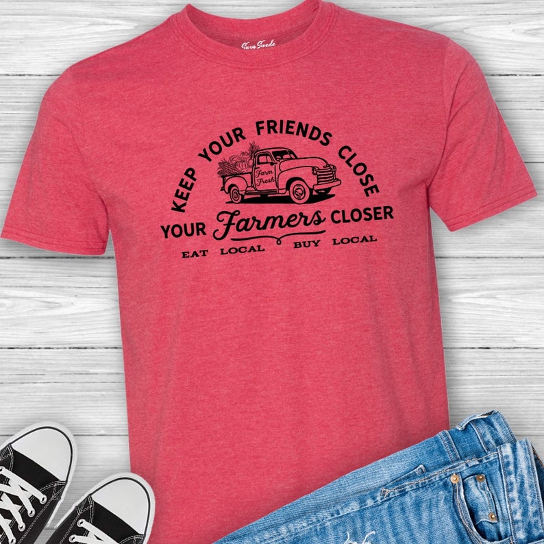 May include: Red t-shirt with a black graphic of a pickup truck filled with produce and the text "Keep your friends close, your farmers closer. Eat local, buy local."