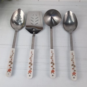 May include: A set of four stainless steel kitchen utensils including a slotted spoon, a spatula, a ladle, and a solid spoon. Each utensil features a white handle decorated with a repeating pattern of small orange flowers and brown leaves.