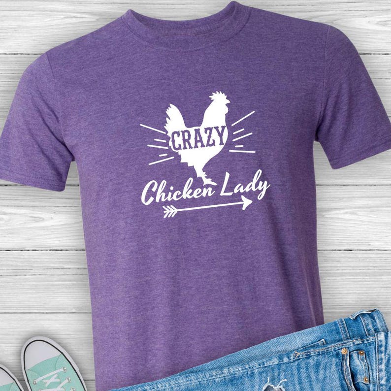 May include: Purple t-shirt with a white silhouette of a chicken and the text "Crazy Chicken Lady" with a white arrow underneath.