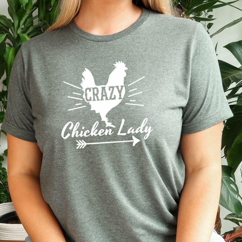 May include: A dark green t-shirt with a white silhouette of a chicken with the text "Crazy Chicken Lady" and an arrow underneath.
