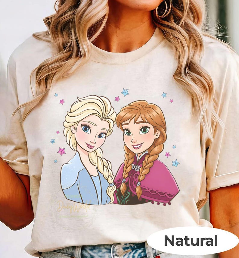 Puede incluir: Camiseta beige con una ilustraci&oacute;n de dibujos animados de dos personajes femeninos con cabello rubio y casta&ntilde;o rojizo, rodeados de estrellas. Los personajes visten atuendos azules y rosas. El texto "Disney World" es visible. La camiseta tiene una etiqueta "Natural".