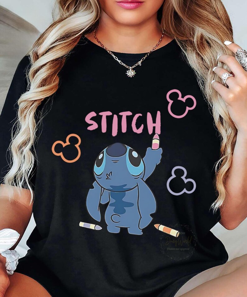 May include: Black t-shirt featuring the word "STITCH" in pink, with a blue cartoon character holding a crayon. Mickey Mouse silhouettes in pink, orange, and purple surround the design. Two crayons are at the bottom.