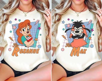 May include: Cream-colored t-shirts featuring cartoon characters Roxanne and Max. Roxanne is depicted with red hair and a book, while Max is shown with black hair and a red outfit. The shirts have a retro design with the text "Her Roxanne" and "Her Max".